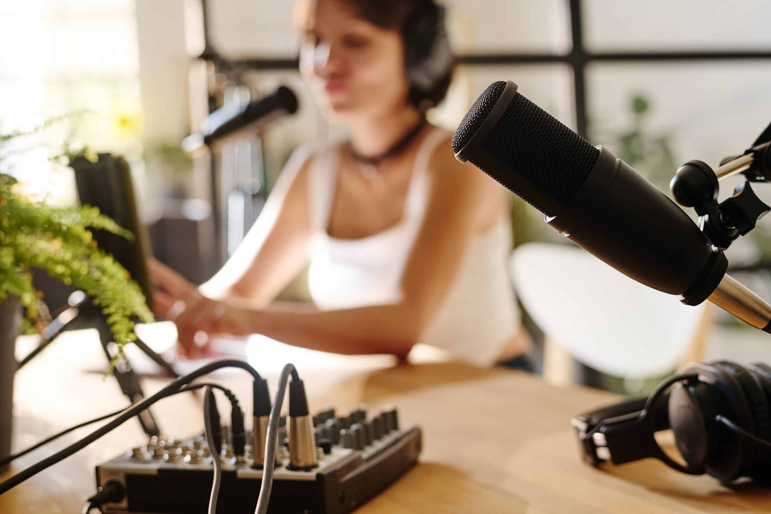 Black microphone and other equipment for recording audio files for podcasting on workplace of host with girl in background