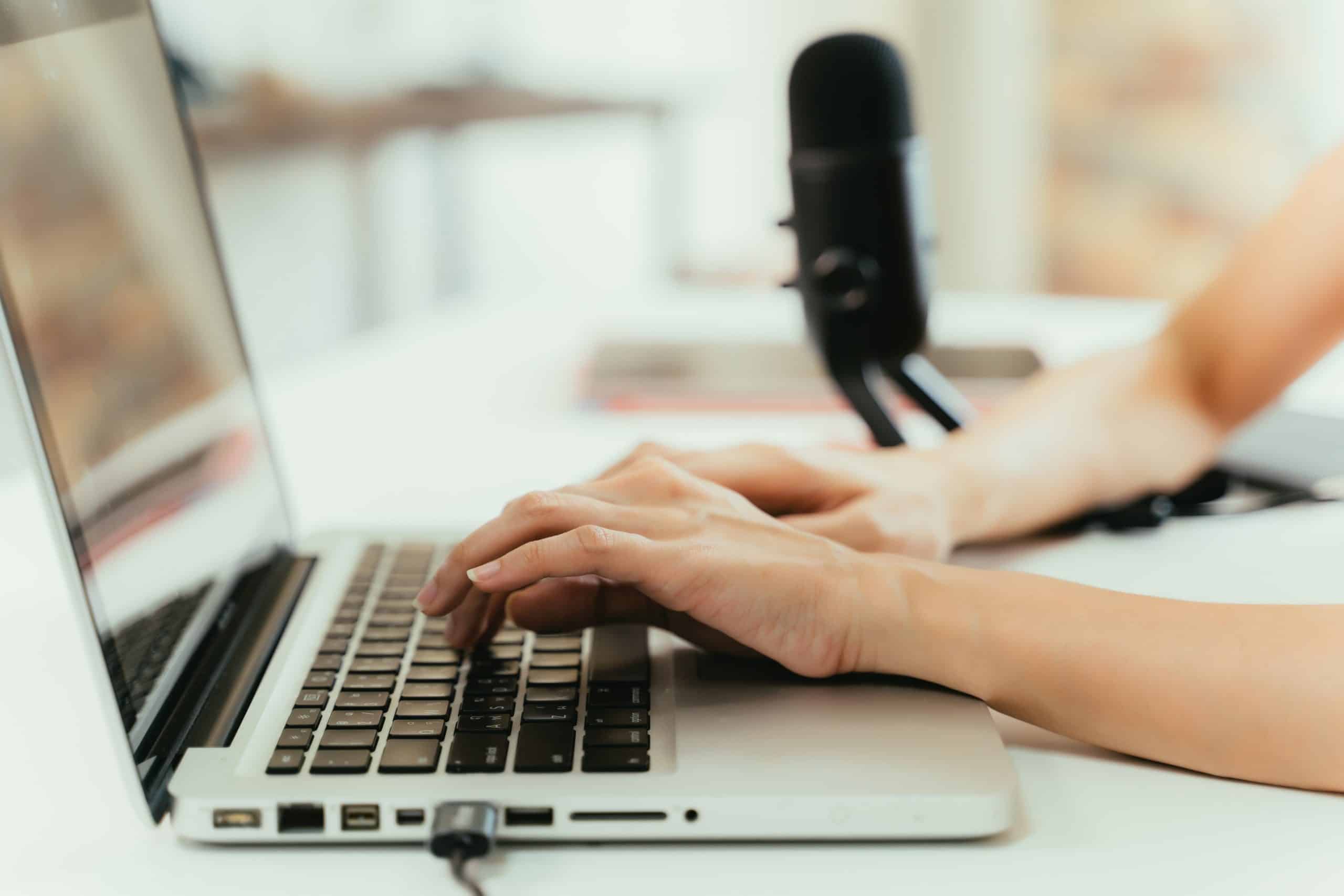 Closeup of hands typing on laptop with microphone in background