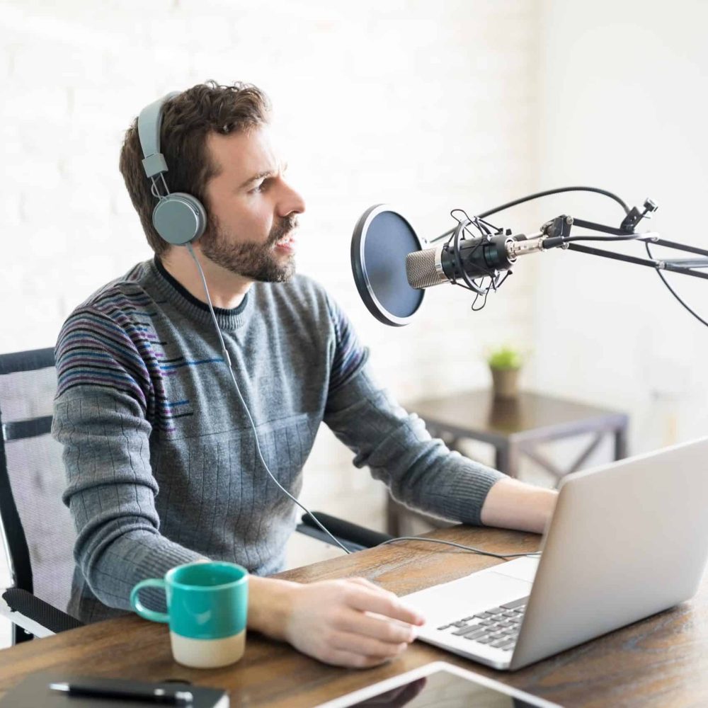 Young man with headphones and laptop talking on mic, online radio.